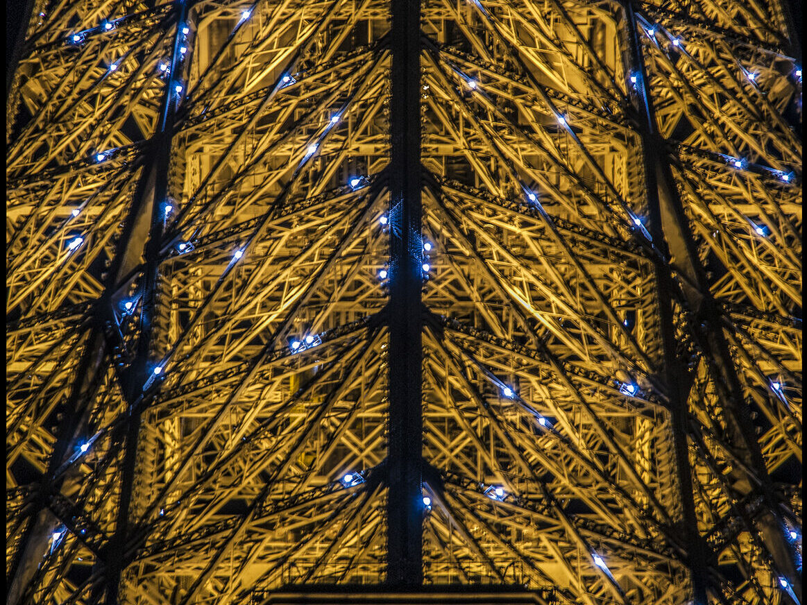 Gros plan sur l'armature de la tout Eiffel avec les lumières clignotantes du début d'heure